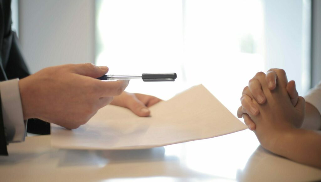 A lender employee holds out a pen and paper for a small business owner to take and sign.