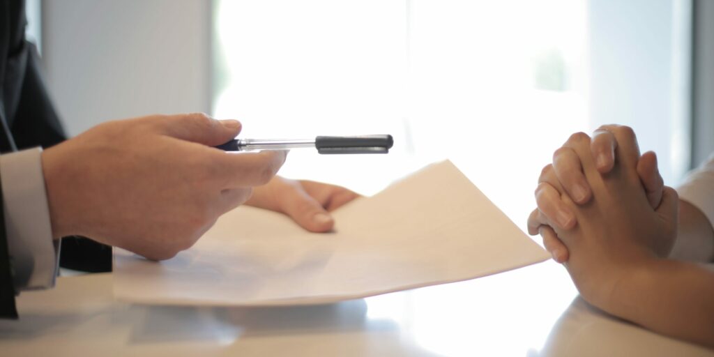 A lender employee holds out a pen and paper for a small business owner to take and sign.