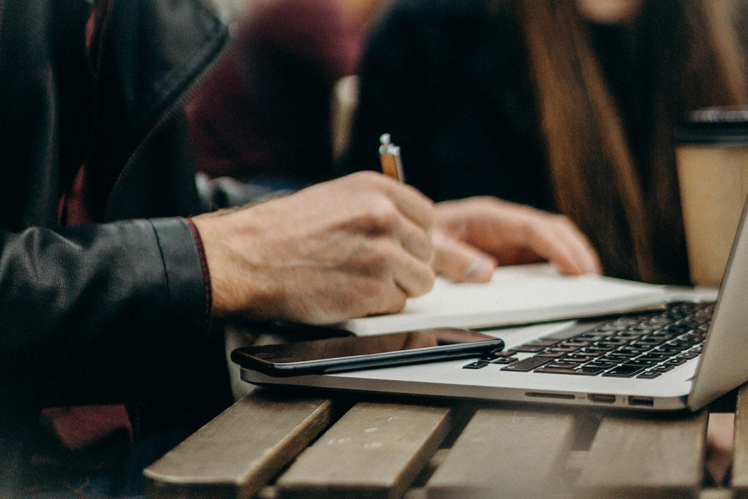 A small business owner wearing a leather jacket taking notes as they research small business loans on their laptop.