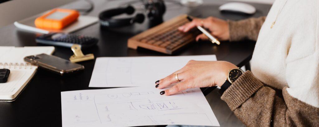 A small business employee is working at a desk, looking at papers and using their computer.