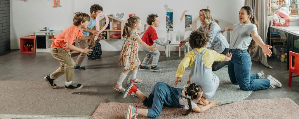 Two daycare workers spreading their arms as children run to give them a hug.