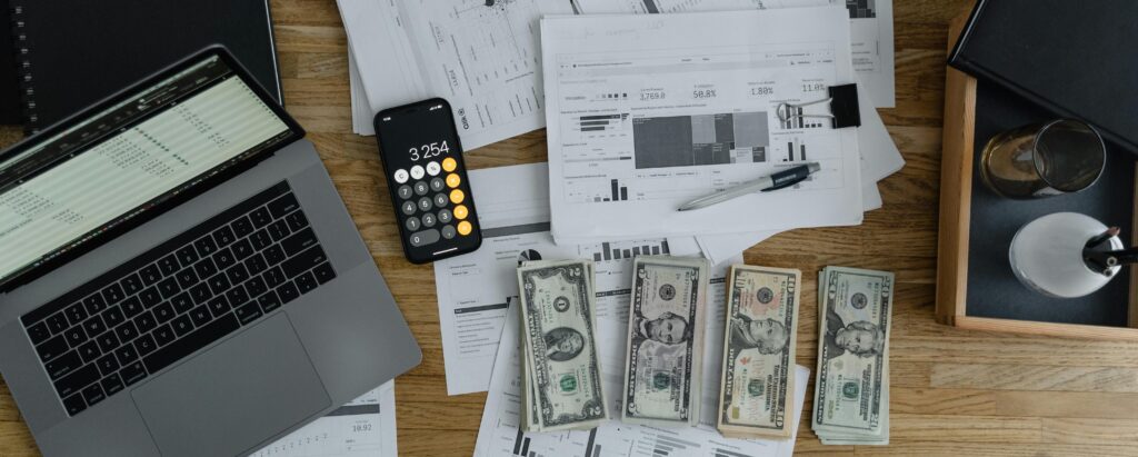 finances-laptop-calculator-cash-seo A desk covered in cash, a laptop, a calculator, and business financial documents.